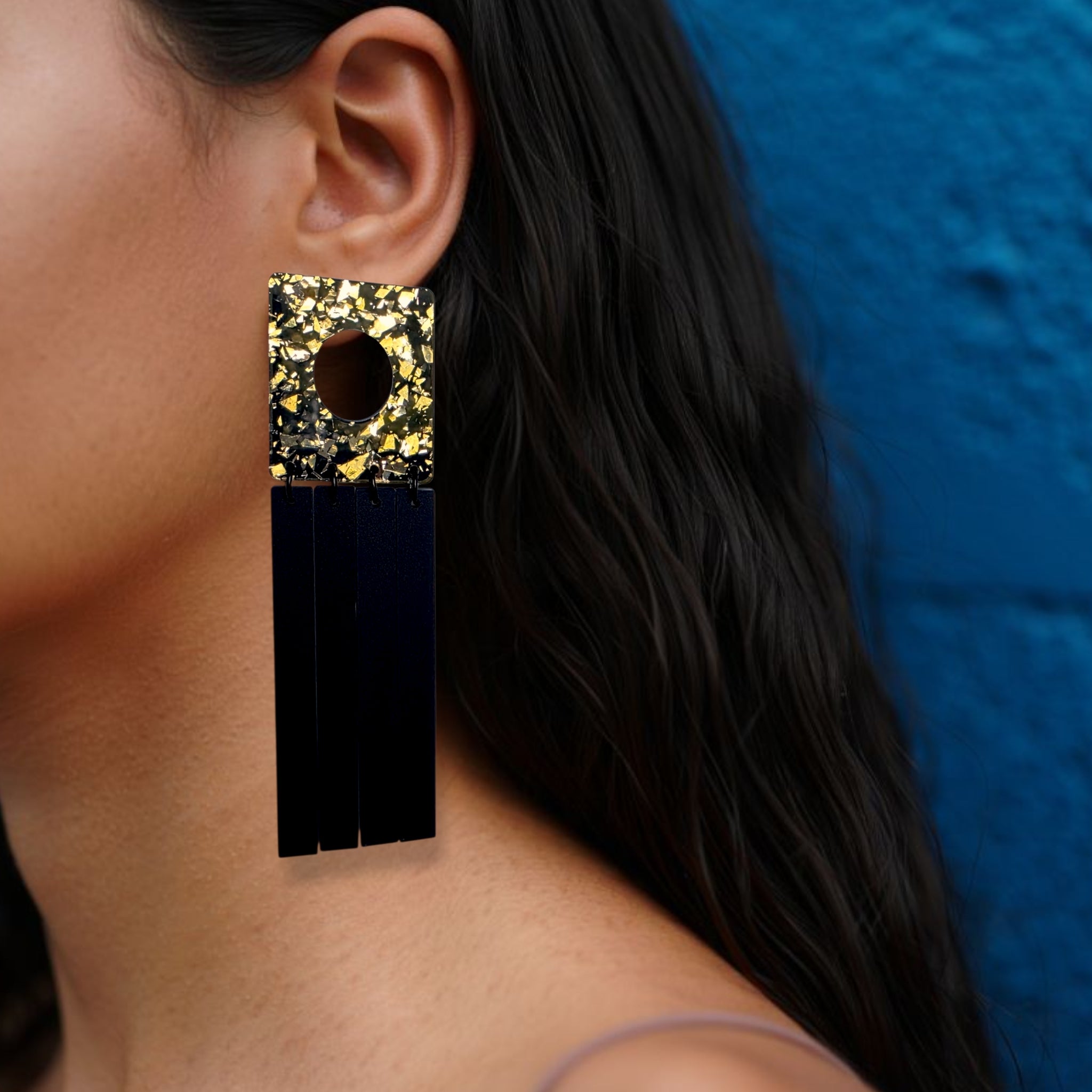Brinco medi geométrico preto e dourado com base quadrada marmorizada usado na orelha de uma mulher