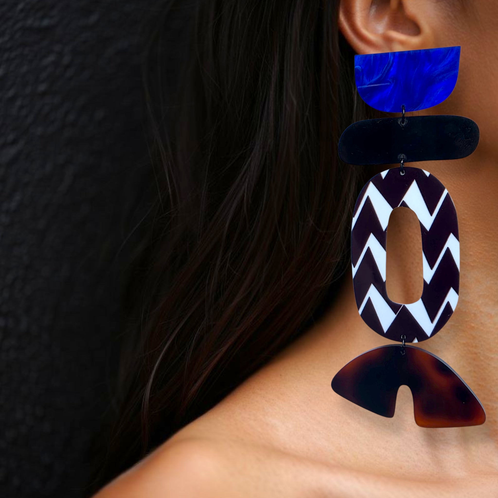 Brinco longo geométrico assimétrico com formas coloridas em preto, branco, azul e tortoise usado na orelha de uma mulher