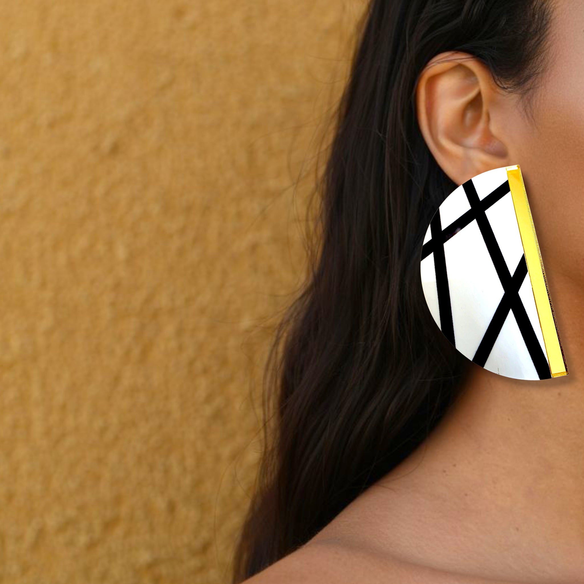 Brinco maxi meia-lua branco com linhas pretas e detalhe dourado usado na orelha de uma mulher