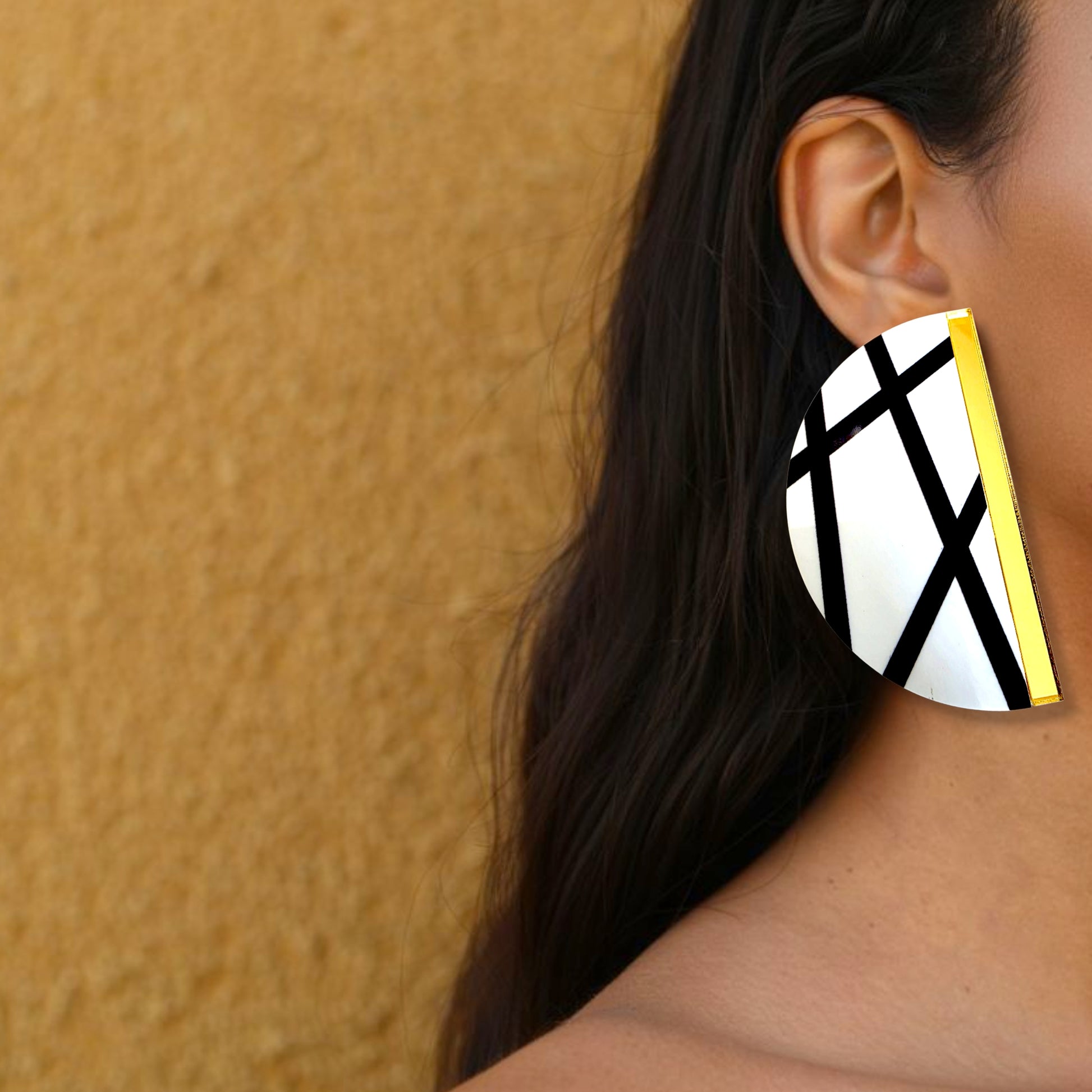 Brinco maxi meia-lua branco com linhas pretas e detalhe dourado usado na orelha de uma mulher