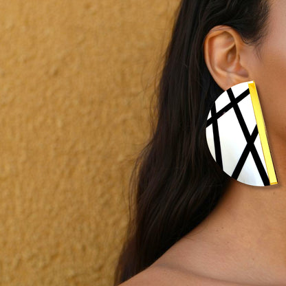 Brinco maxi meia-lua branco com linhas pretas e detalhe dourado usado na orelha de uma mulher
