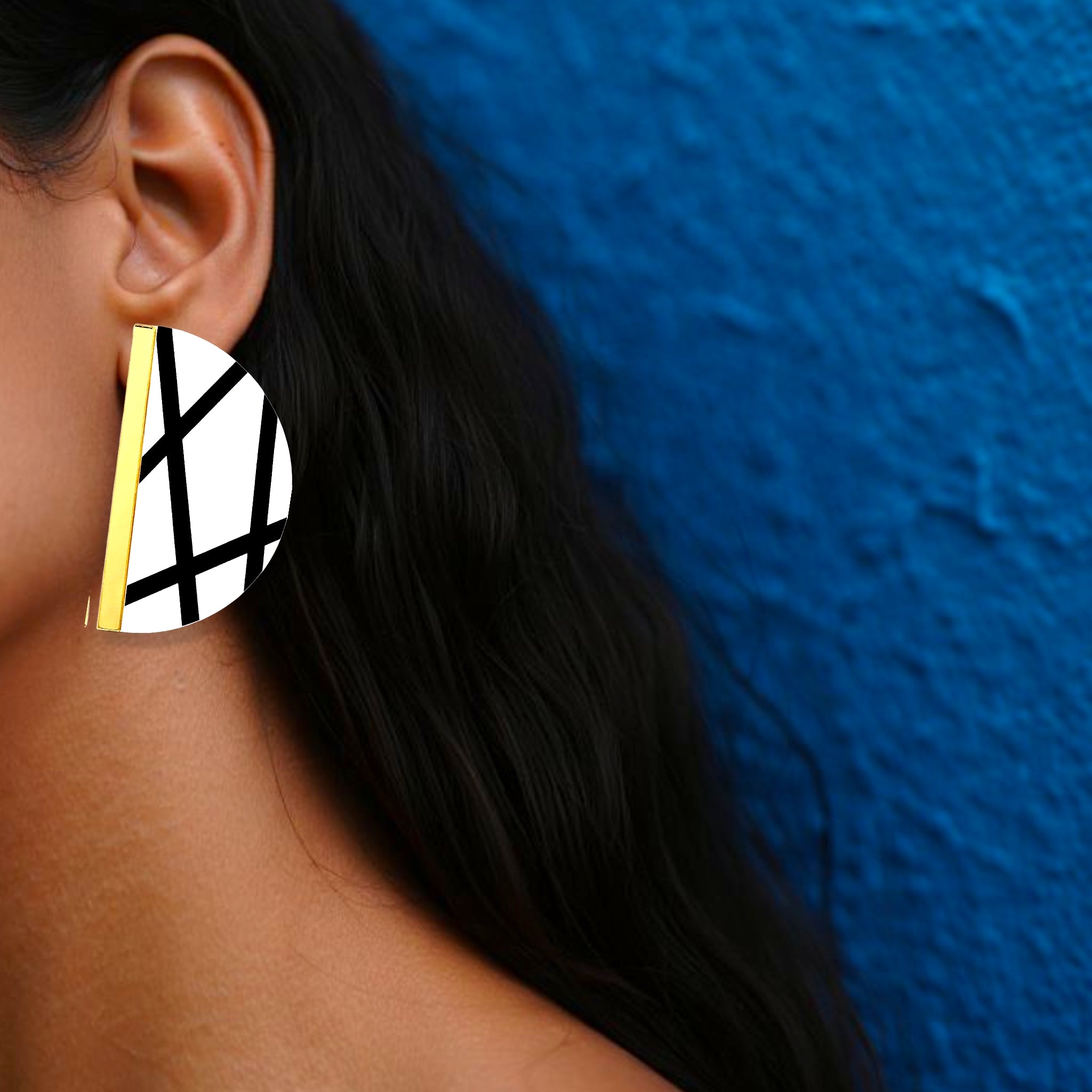 Brinco médio meia-lua branco com linhas pretas e detalhe dourado usado na orelha de uma mulher