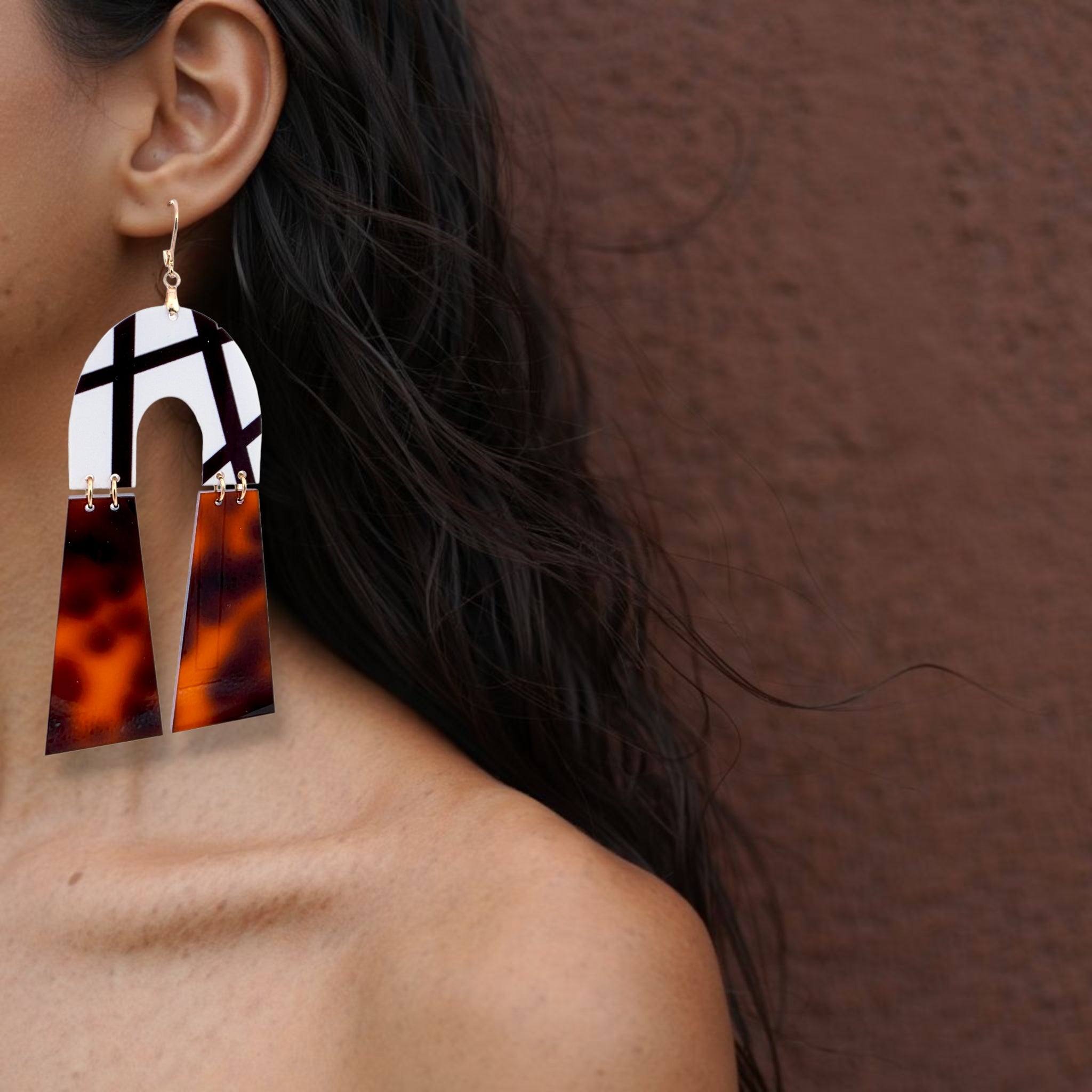 Brinco statment geométrico com padrão tartaruga castanho e detalhe branco usado na orelha de uma mulher
