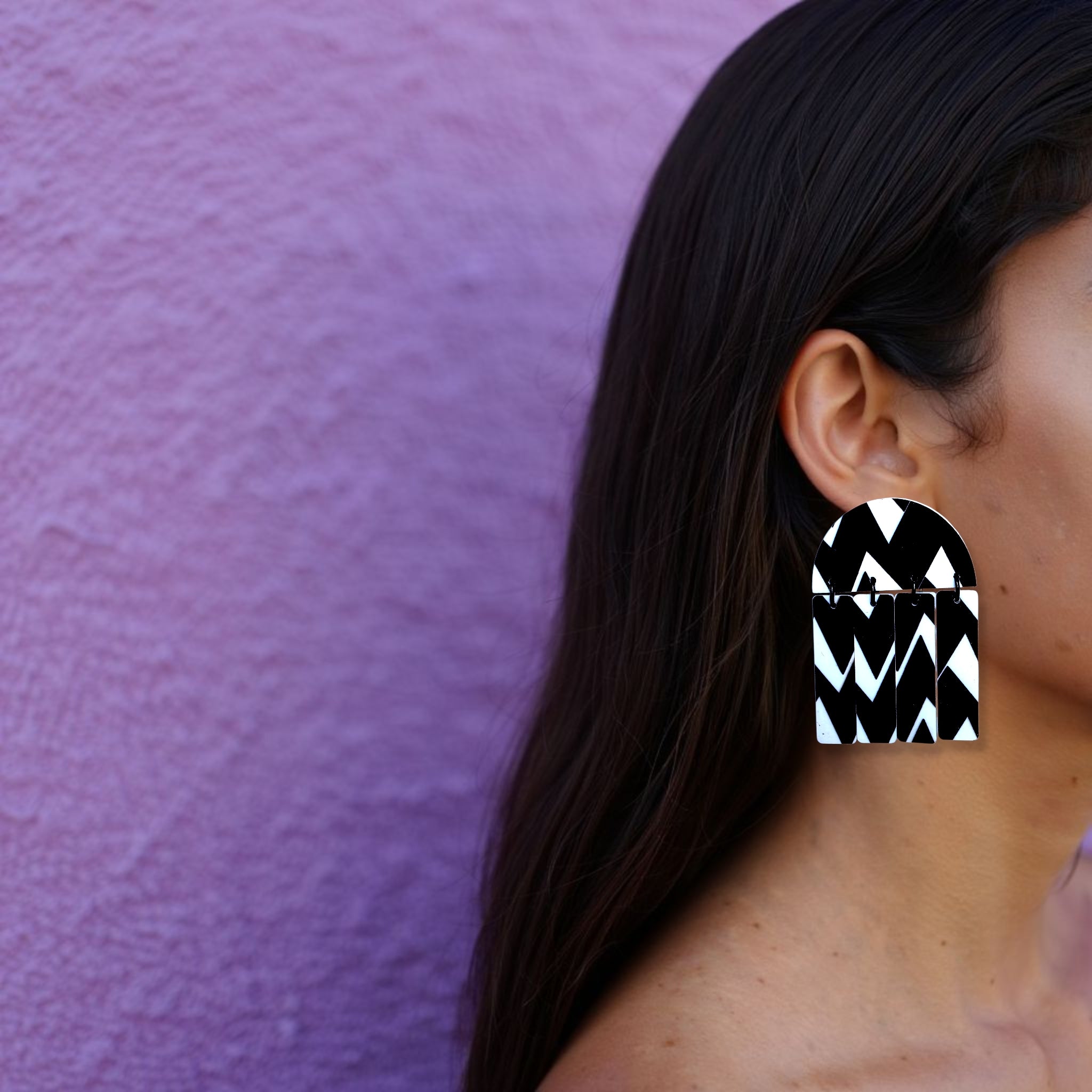 Brinco médio geométrico preto e branco com padrão zigue-zague usado na orelha de uma mulher