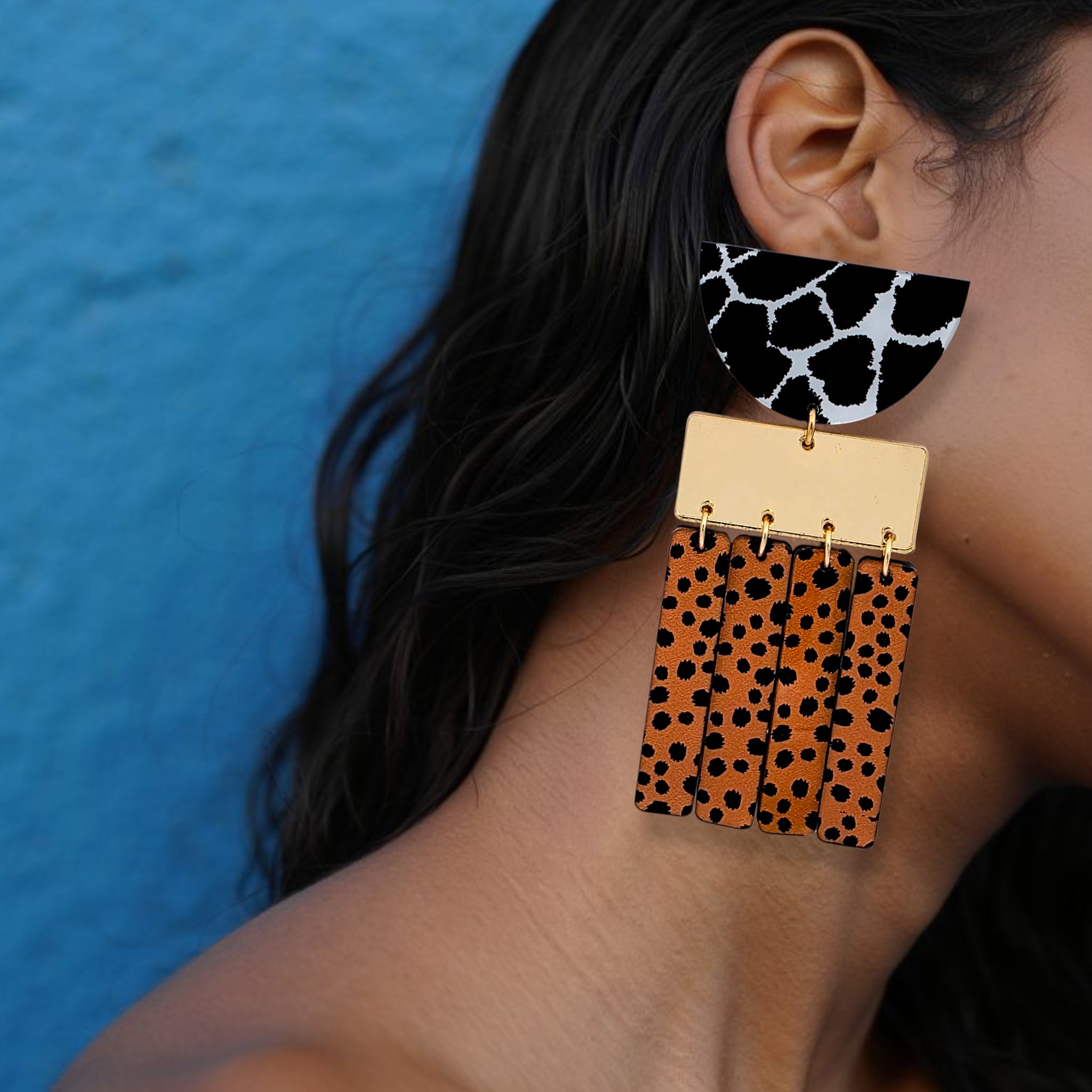 Brinco grande geométrico com estampa animal print em preto, branco e laranja usado na orelha de uma mulhe