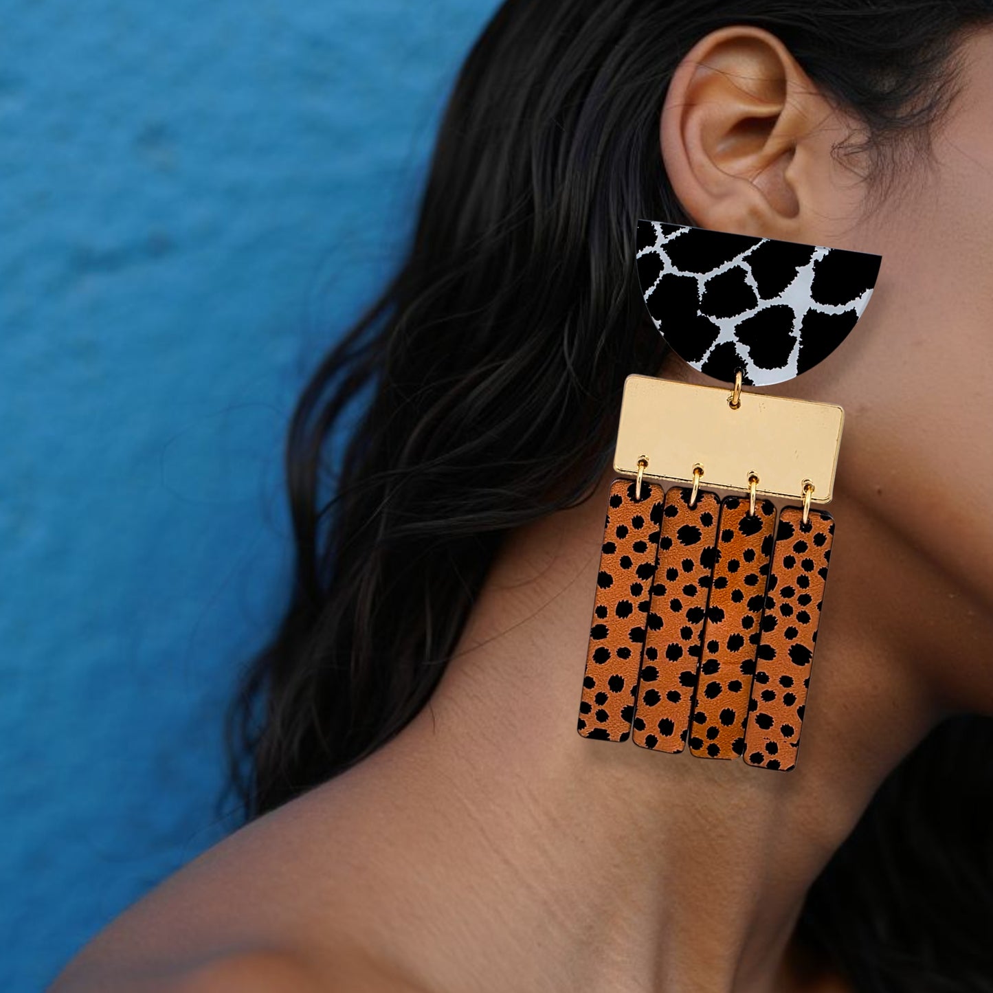 Brinco grande geométrico com estampa animal print em preto, branco e laranja usado na orelha de uma mulhe