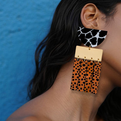 Brinco grande geométrico com estampa animal print em preto, branco e laranja usado na orelha de uma mulhe