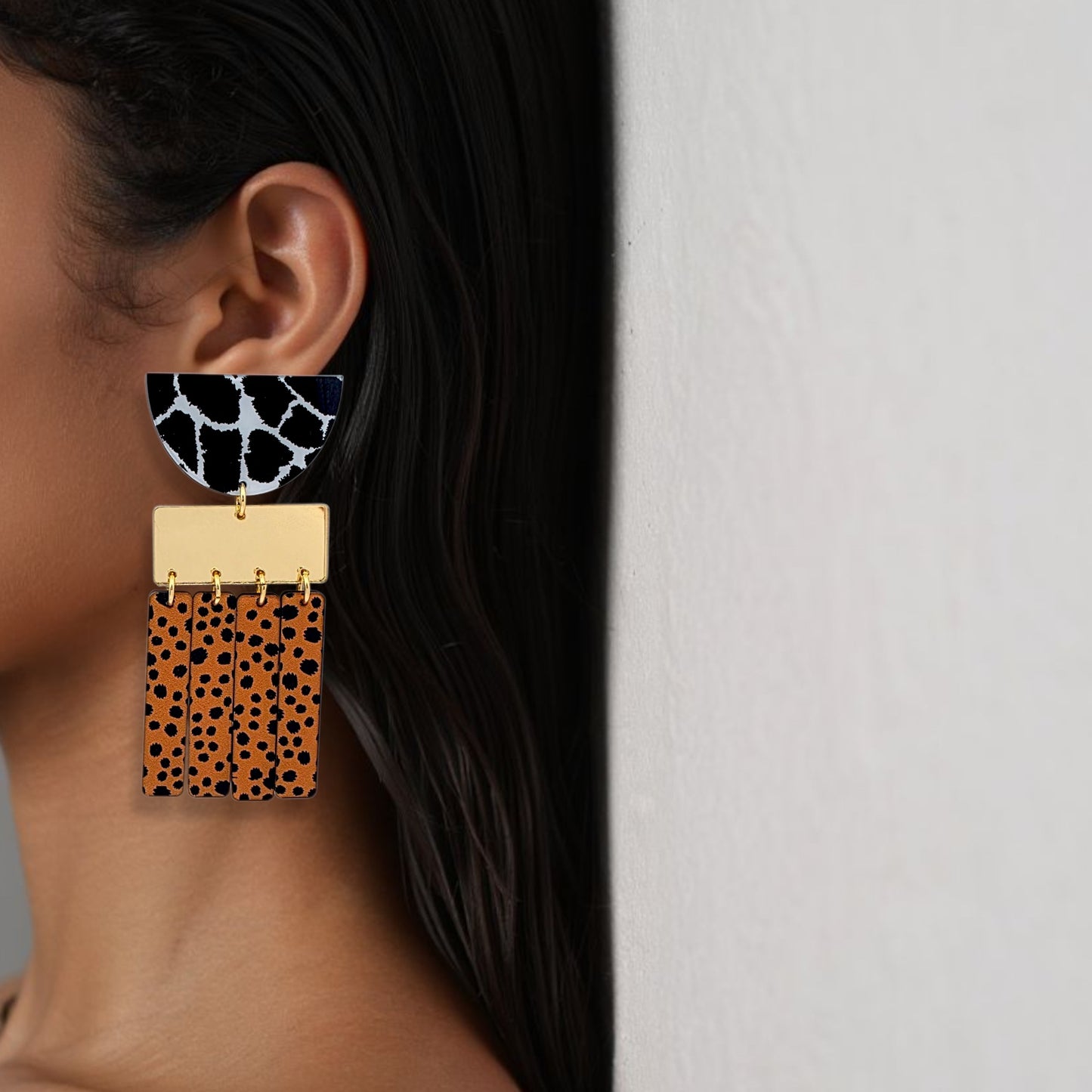 Brinco médio geométrico com estampa animal print em preto, branco e laranja usado na orelha de uma mulhe