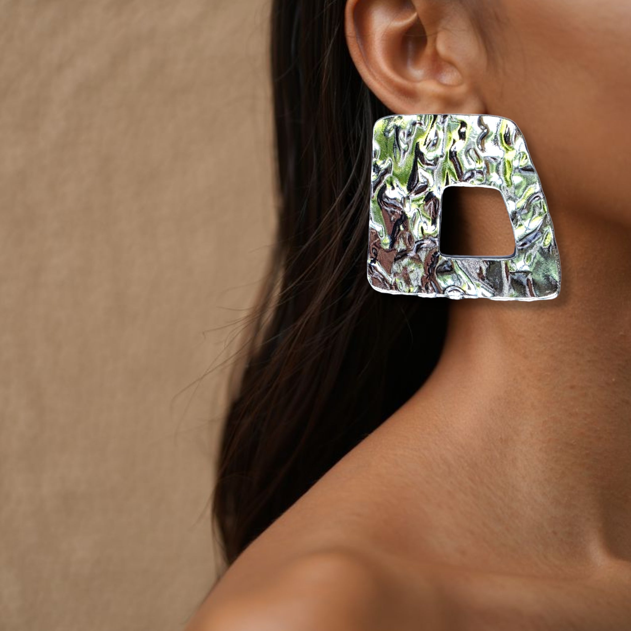 Brinco médio prateado com textura martelada e recorte geométrico usado na orelha de uma mulher