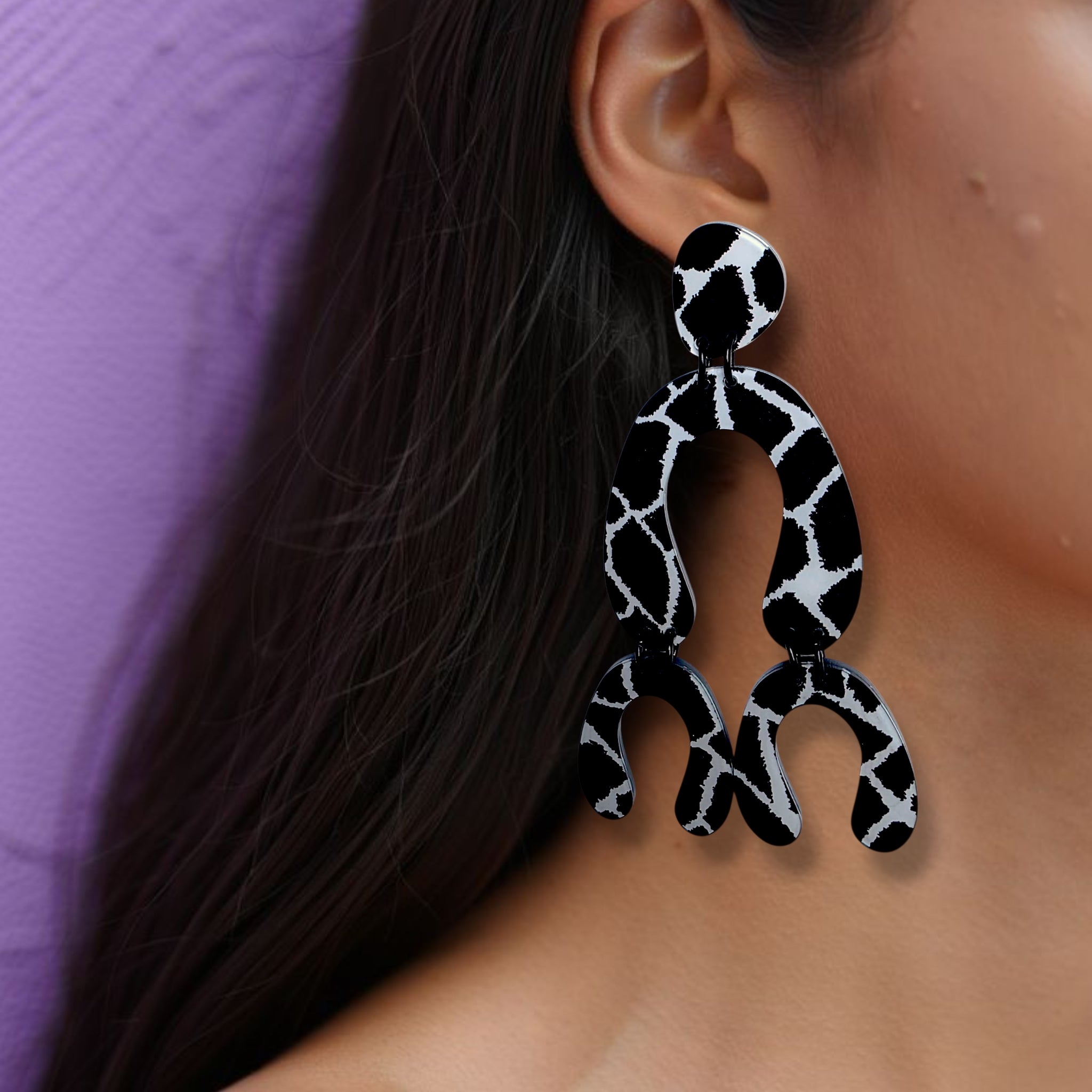 Brinco médio longo articulado com estampa preto e branco tipo girafa usado na orelha de uma mulher
