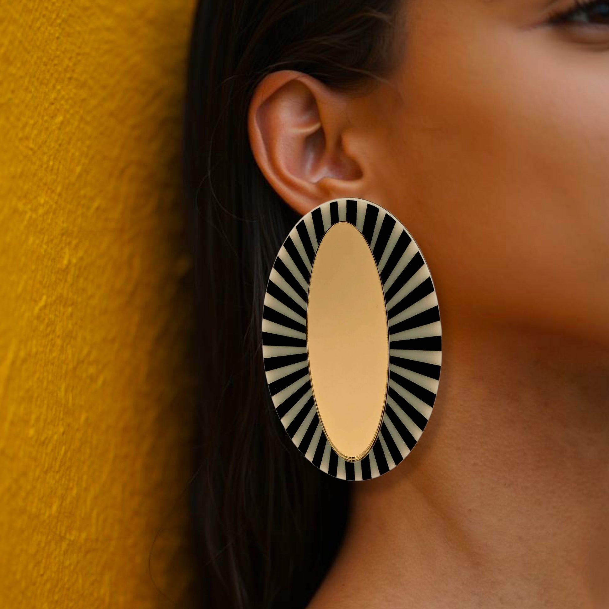 Brinco maxi oval dourado com detalhe listrado preto e branco em visual elegante