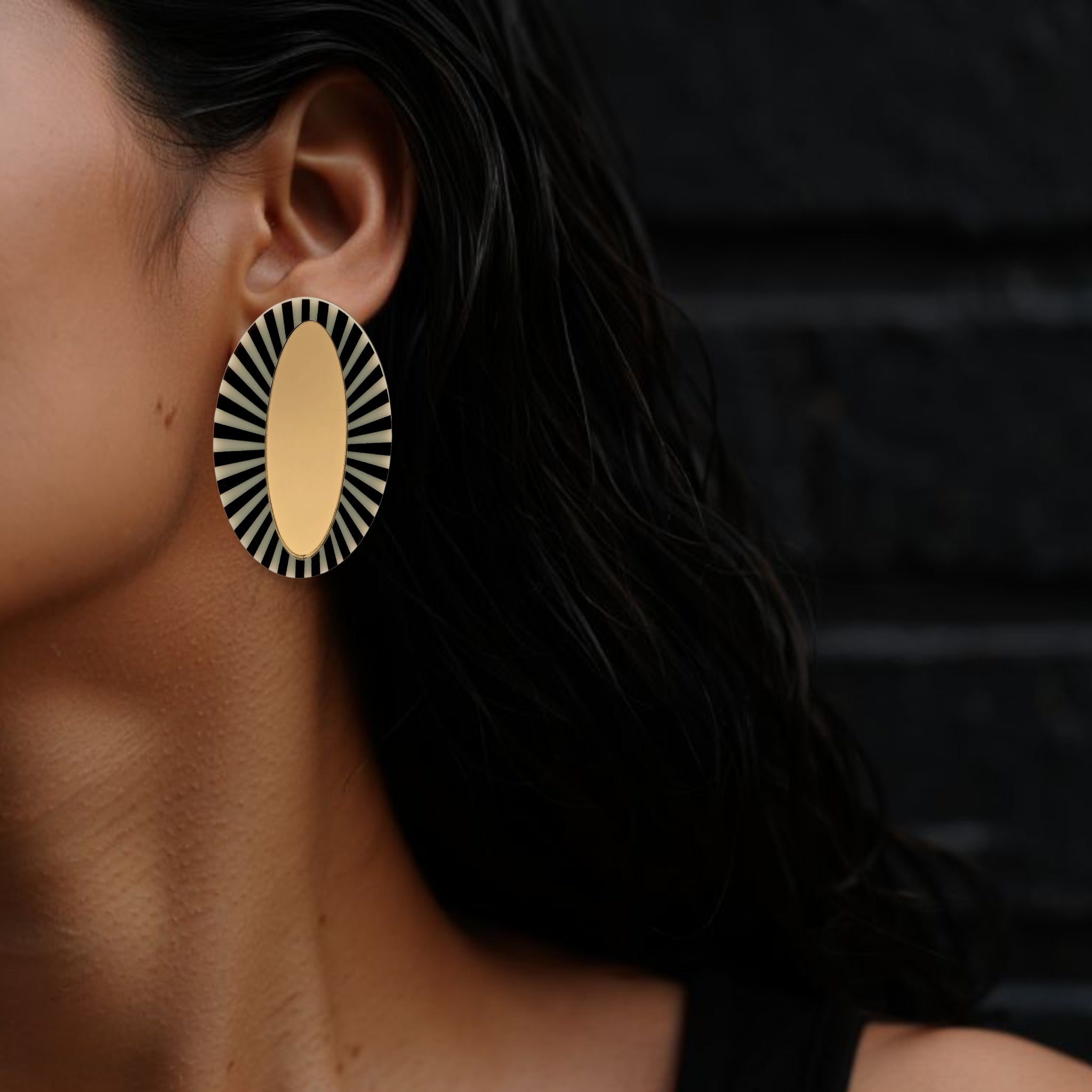 Brinco oval dourado médio com borda listrada preta e branca usado na orelha de uma mulher