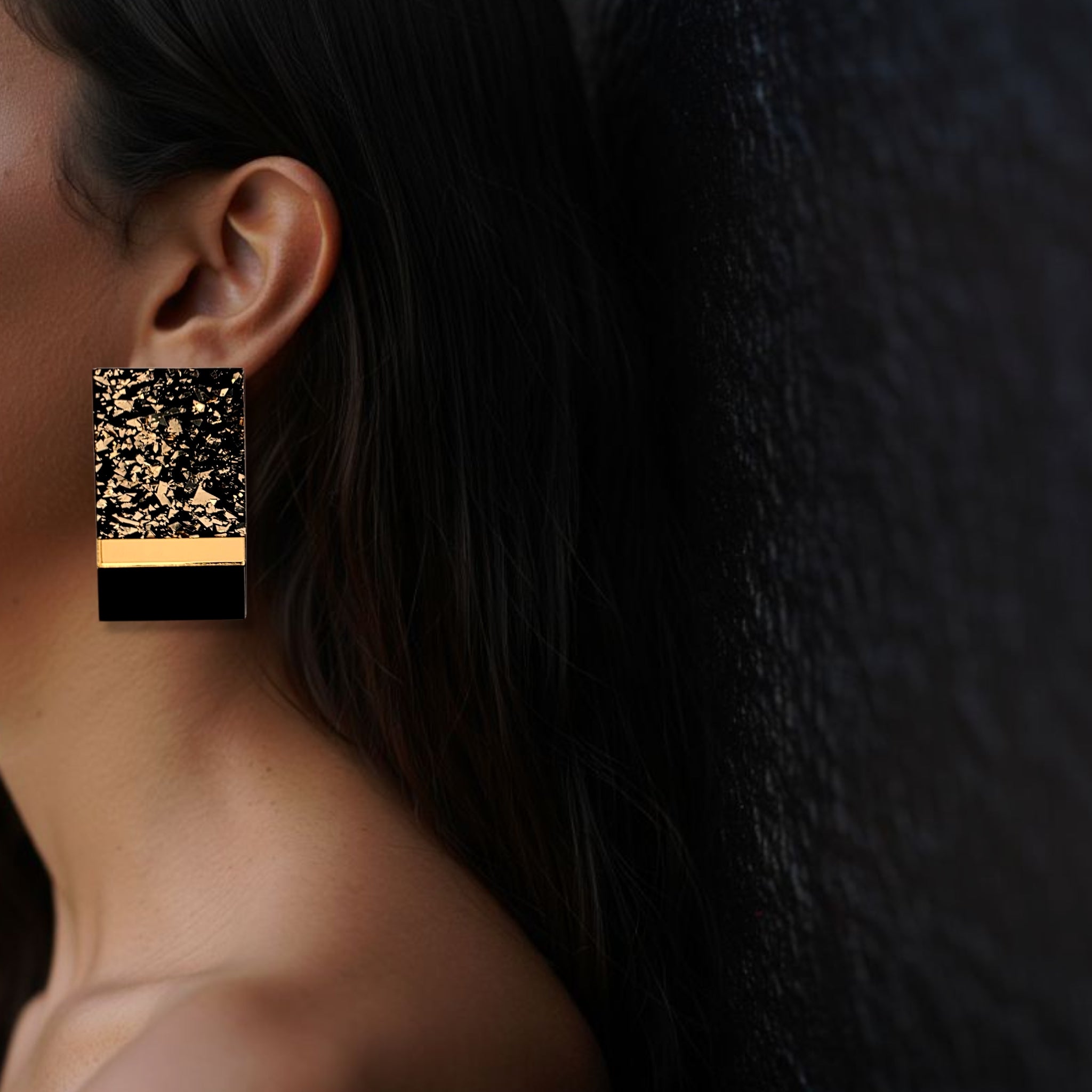 Brinco médio retangular preto e dourado marmorizado usado na orelha de uma mulher