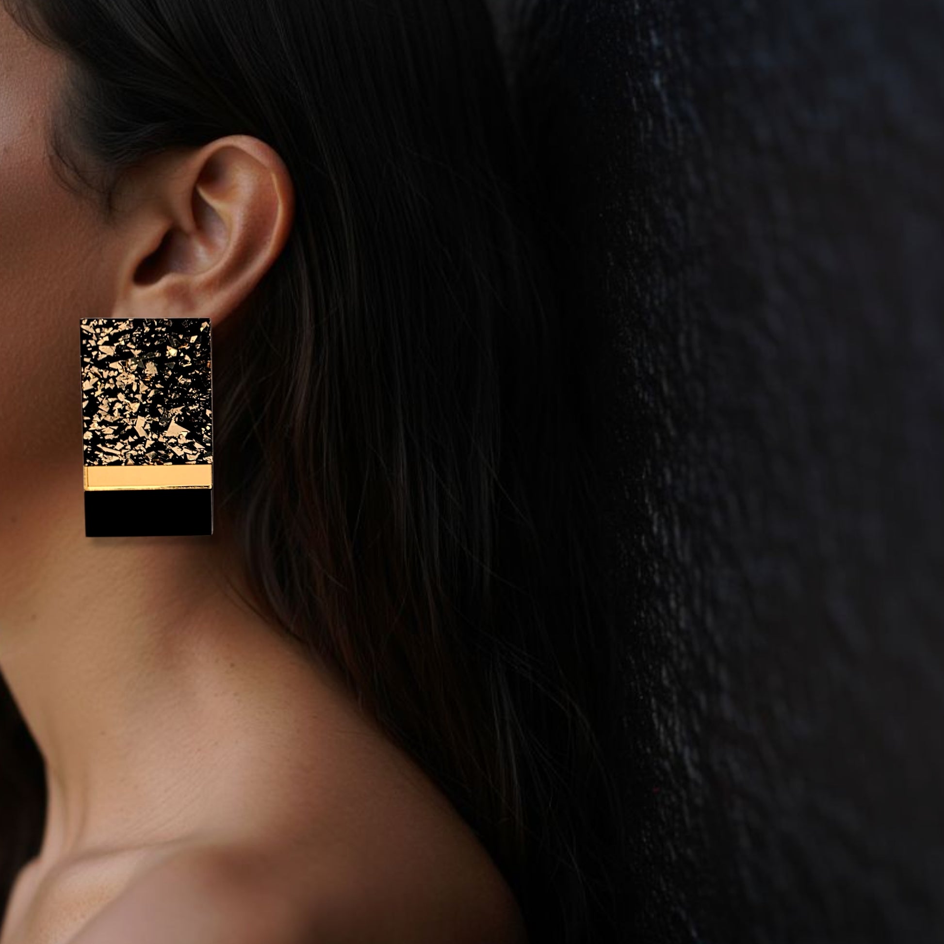 Brinco médio retangular preto e dourado marmorizado usado na orelha de uma mulher